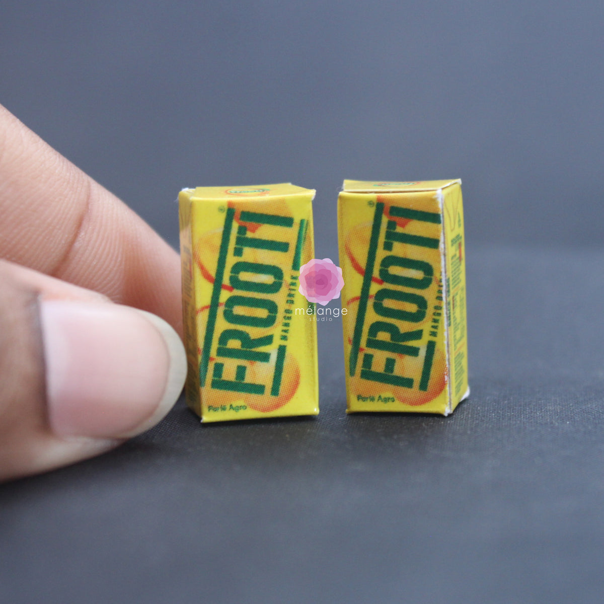 Two miniature yellow mango drink cartons held between fingers