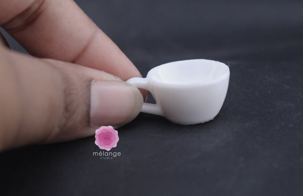 White resin miniature coffee cup and saucer held between fingers