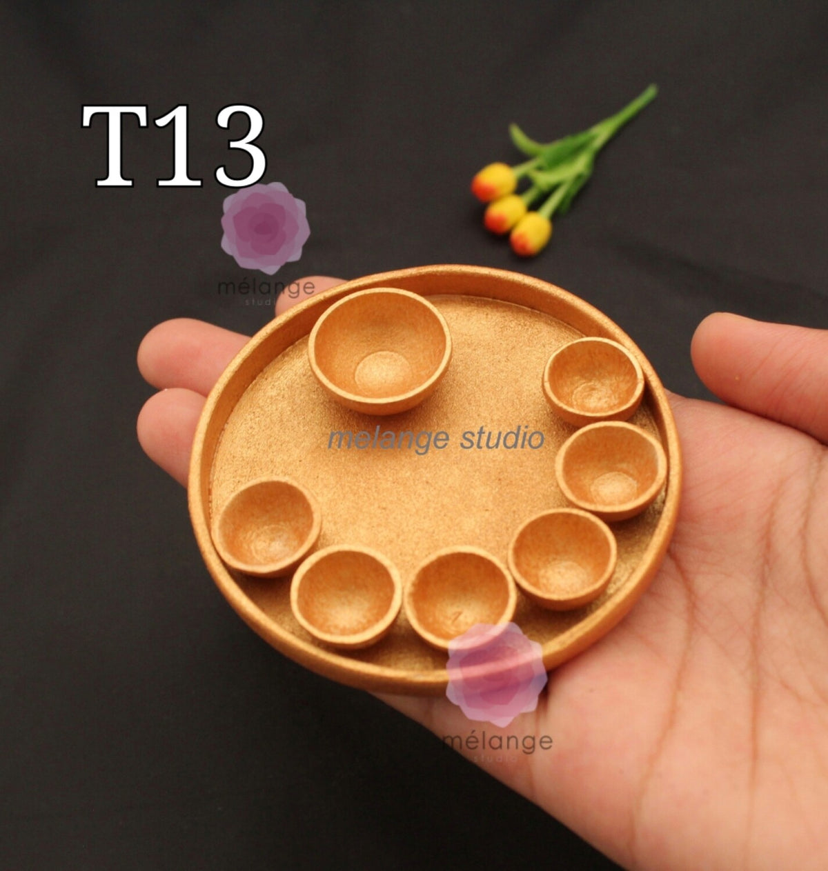 Gold miniature thali plate with seven katori wells, held in a hand