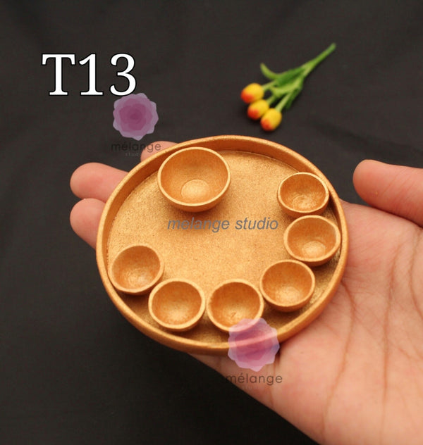Gold miniature thali plate with seven katori wells, held in a hand