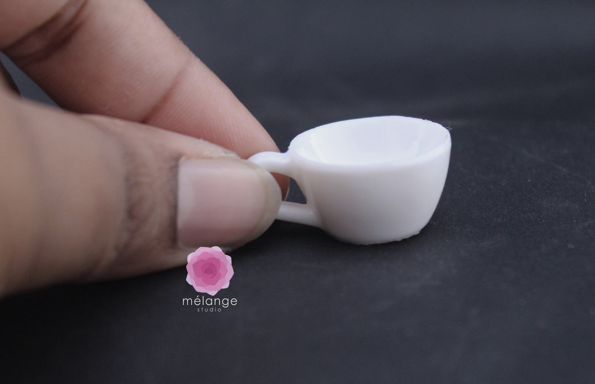 White resin miniature coffee cup and saucer held between fingers