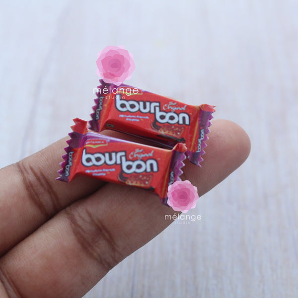 Two miniature red chocolate cream biscuit packets held in a hand