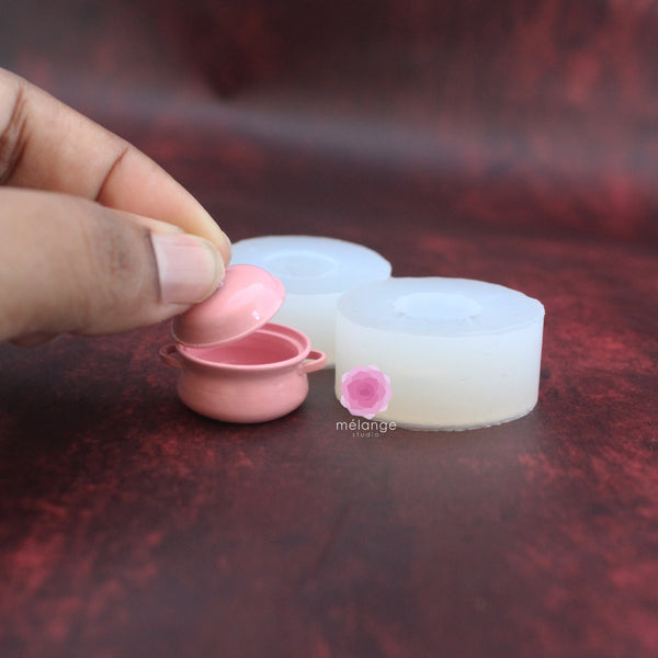 Pink cast miniature casserole dish and lid beside white silicone moulds